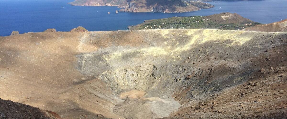 A volcanic landscape with a crater, distant islands, and a clear sky.