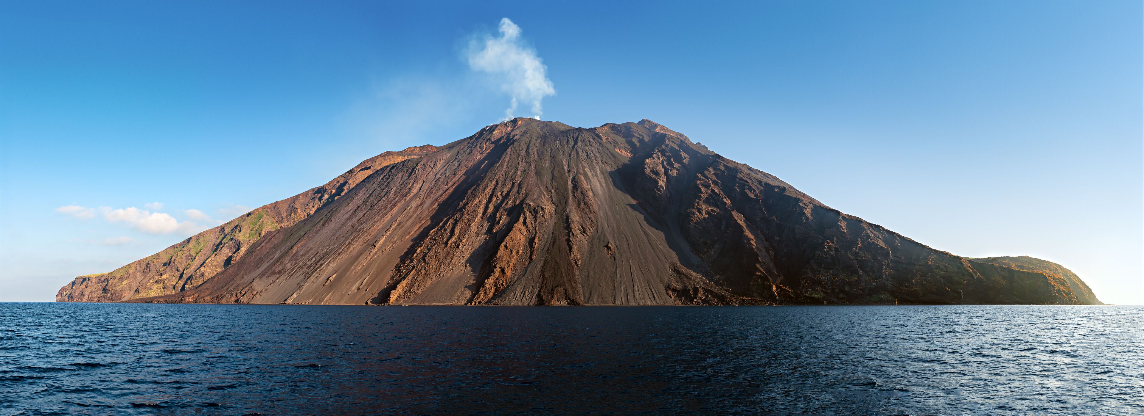 The stromboli vulcano erupting on the &quot;Sciara del Fuoco&quot; north west side, day shot, blue sky background, panoramic shot, eolians islands, sicily, italy