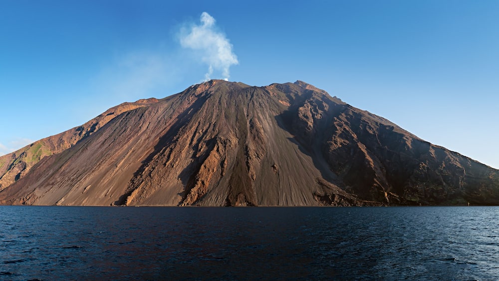 The stromboli vulcano erupting on the "Sciara del Fuoco" north west side, day shot, blue sky background, panoramic shot, eolians islands, sicily, italy