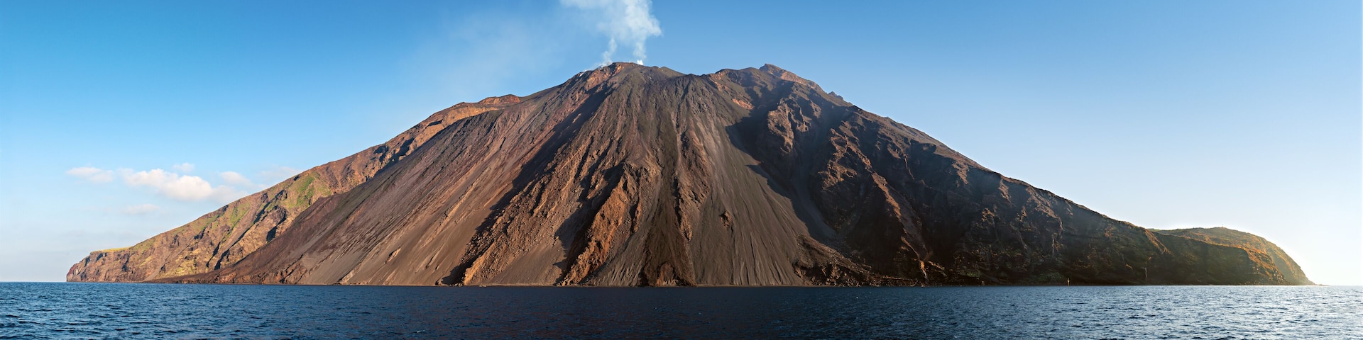 The stromboli vulcano erupting on the "Sciara del Fuoco" north west side, day shot, blue sky background, panoramic shot, eolians islands, sicily, italy