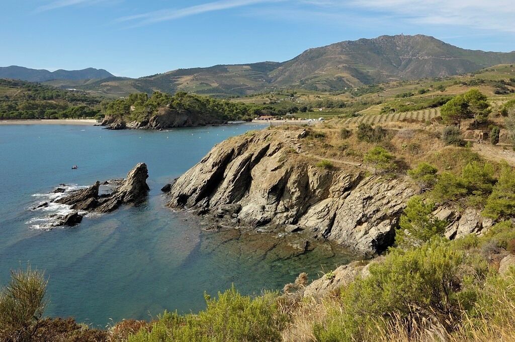 A coastal landscape with rocky cliffs, clear blue water, and distant mountains.