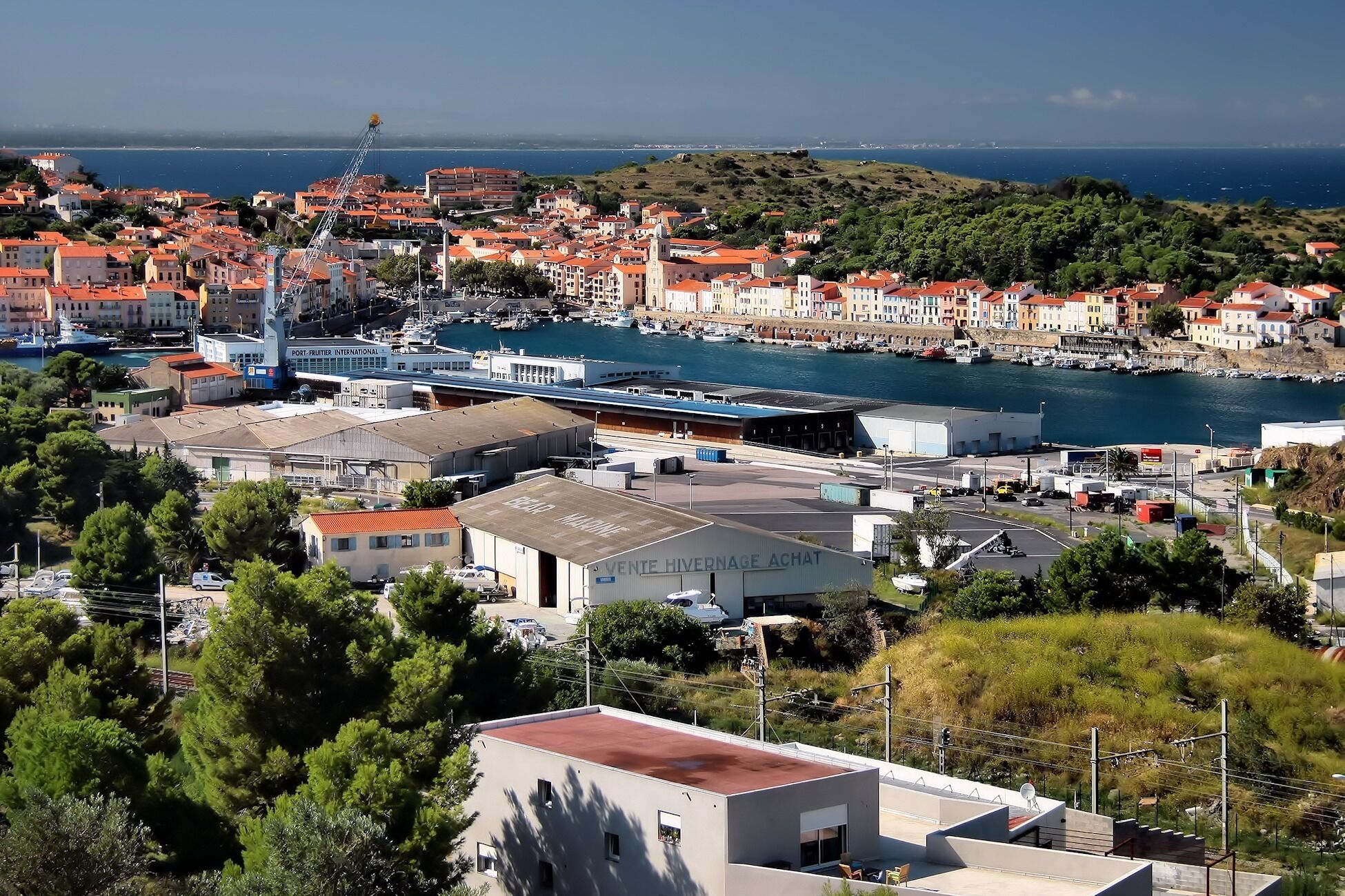 A coastal town with a marina, buildings with red roofs, and a Ferris wheel.