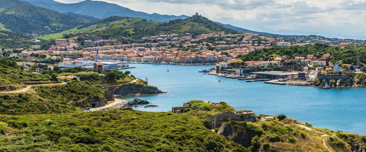 A coastal town with a harbor, historic buildings, and a mountain in the background.