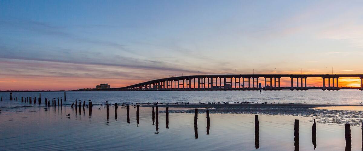 A sunset over a bridge with birds on the shore.