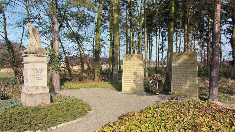 A memorial site with stone monuments and a path surrounded by trees.