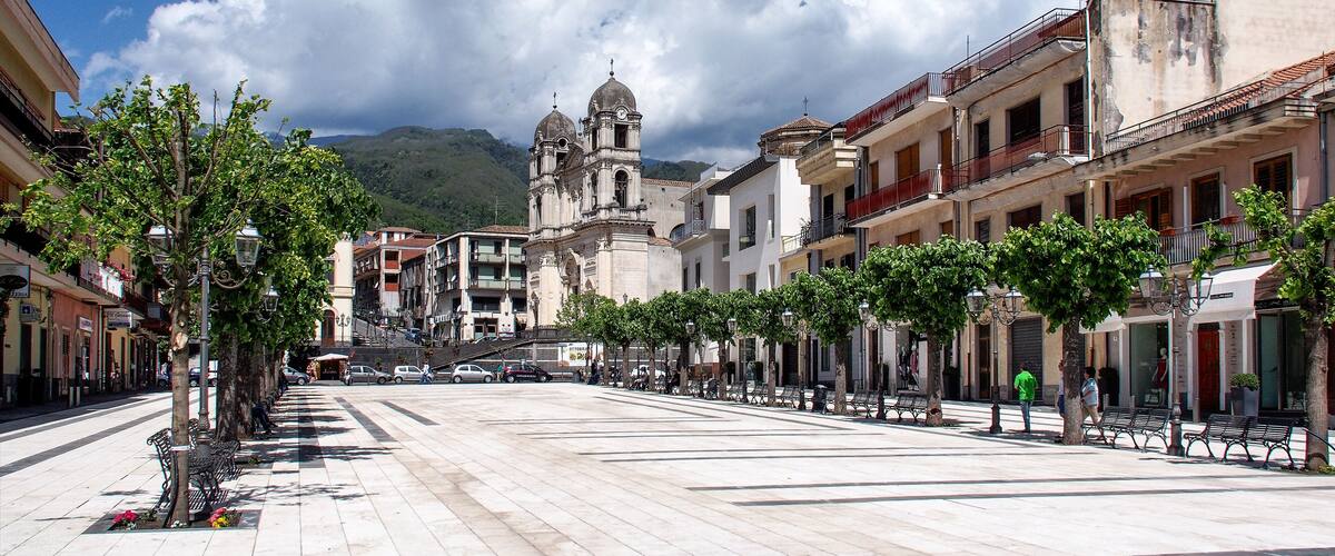 A plaza with a historic church, trees lining the street, and buildings in the background.