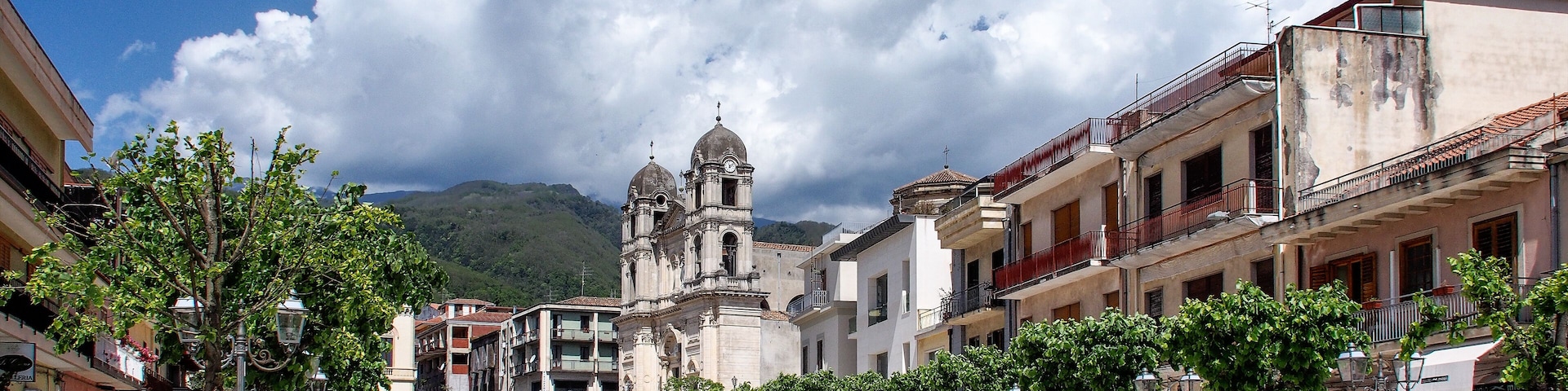 A plaza with a historic church, trees lining the street, and buildings in the background.