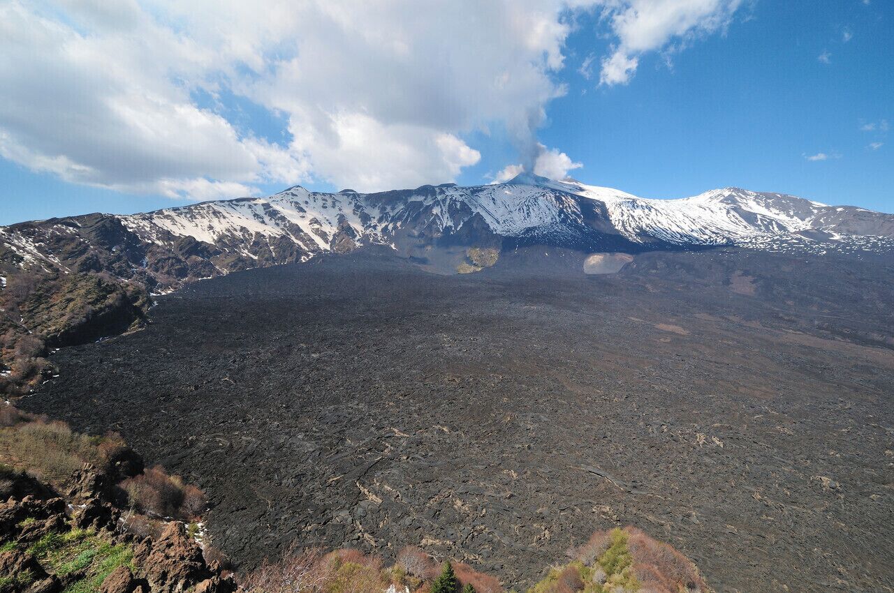 A snow-capped mountain with a dark, barren foreground.