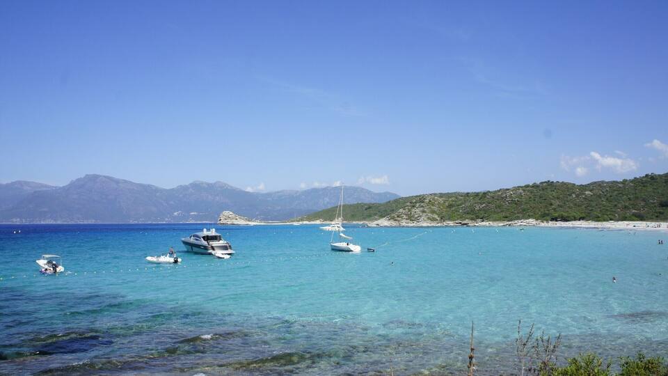 A coastal scene with clear turquoise waters, boats, and a distant mountain range.