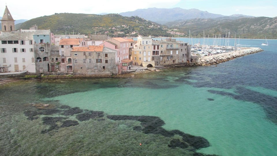 A coastal town with colorful buildings, a rocky breakwater, and a clear blue sea.