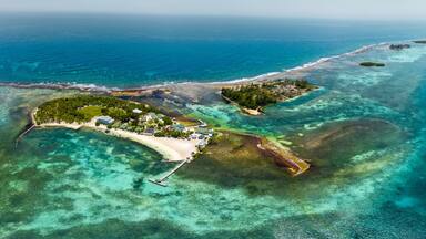Aerial view of a tropical island with turquoise coral reefs, white sand beaches, and lush palm trees in Guanaja, Bay Islands Department, Honduras.