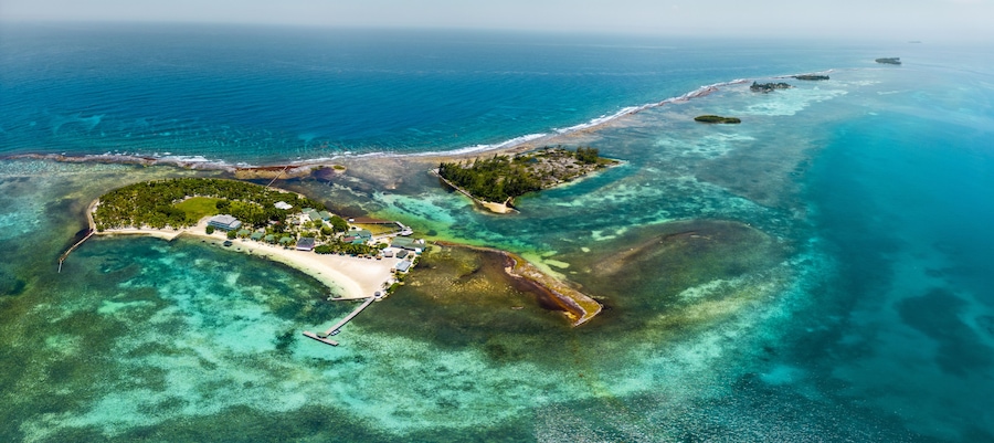 Vista aérea de una isla tropical con aguas turquesas cristalinas, una playa de arena y un pequeño muelle.