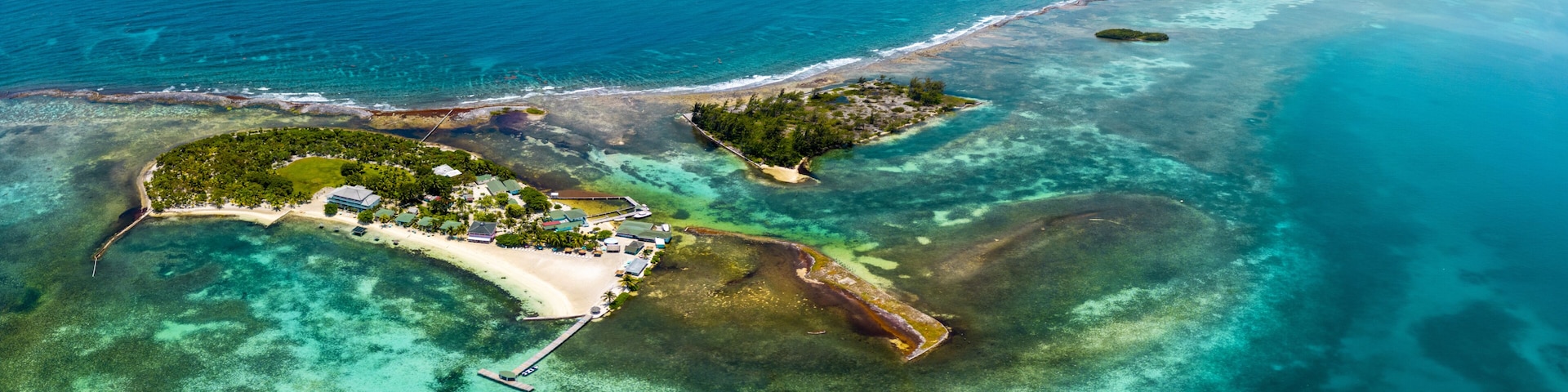 Vista aérea de una isla tropical con aguas turquesas cristalinas, una playa de arena y un pequeño muelle.