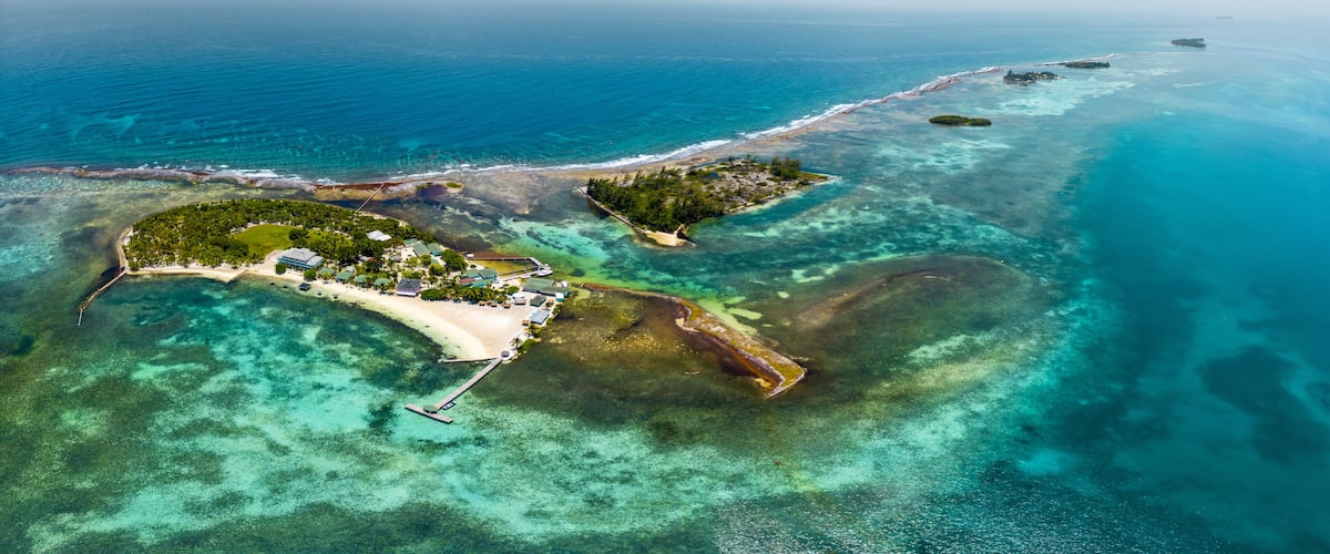 An aerial view of a tropical island with clear turquoise waters, a sandy beach, and a small dock.