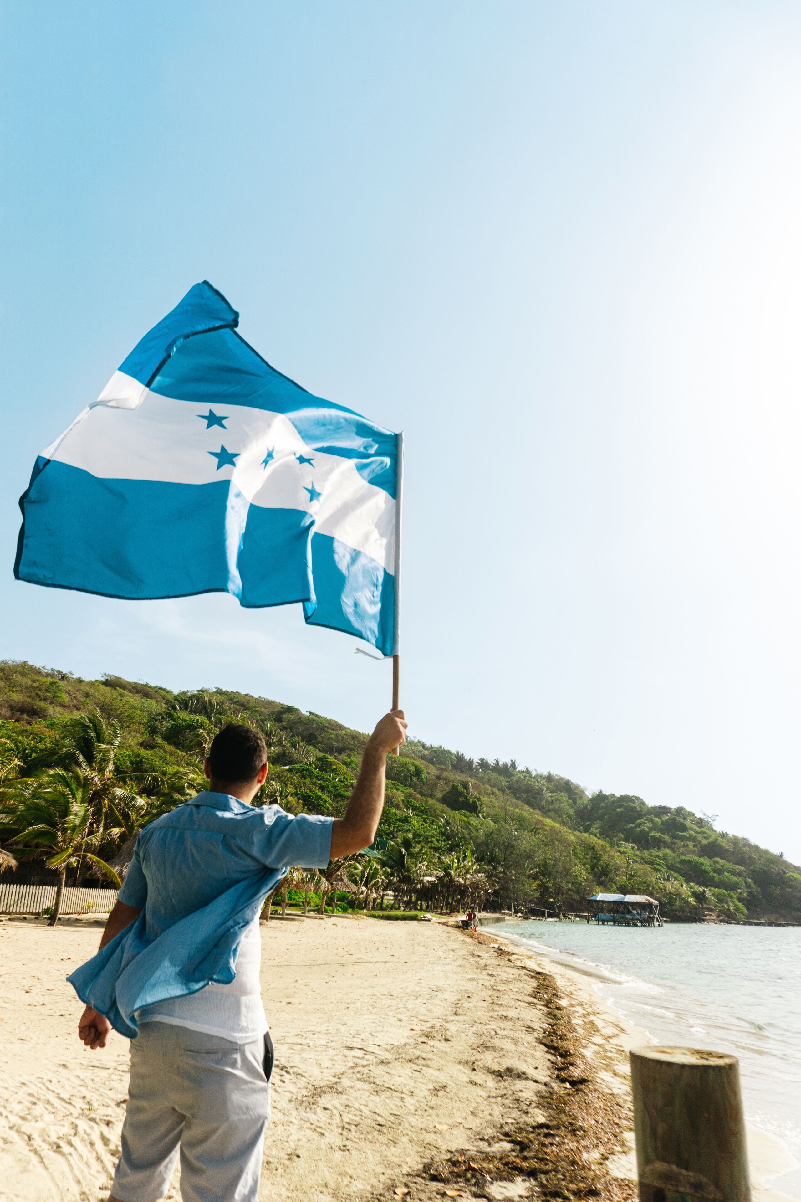 A person holding and waving honduras flag in a beach. Patriotism concept.
