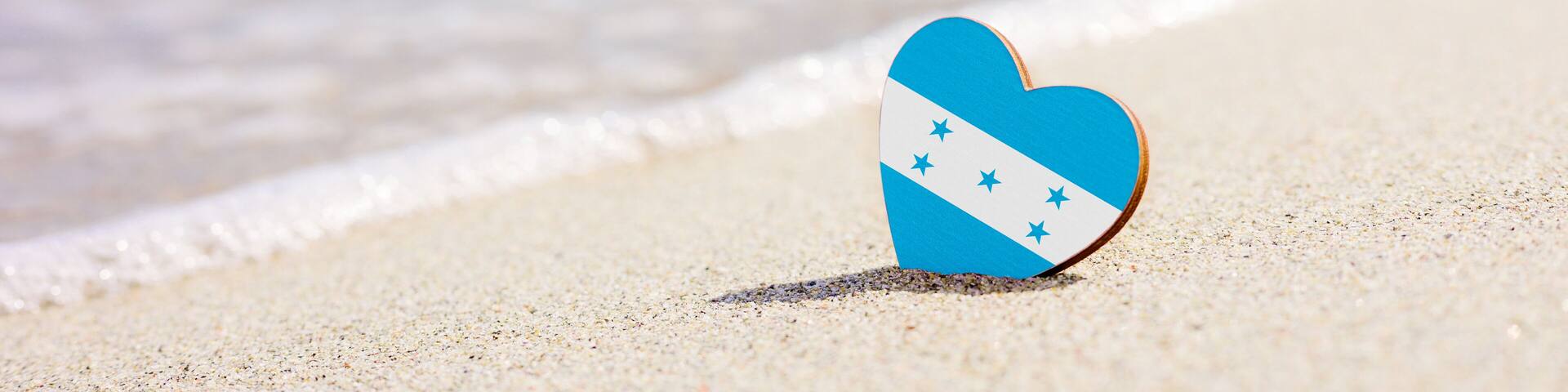 Flag of Honduras in the shape of a heart on a sandy beach. The concept of the best vacation in Honduras resorts.