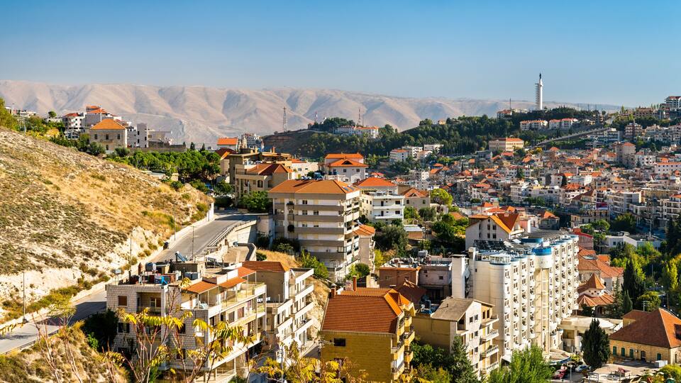 A coastal town with terraced buildings, a prominent lighthouse, and a hilly backdrop.