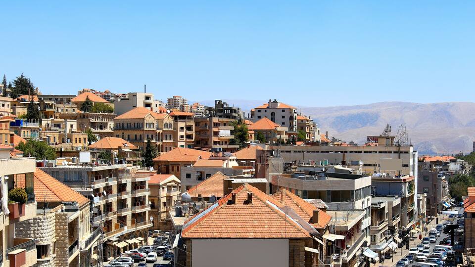 A densely packed urban area with terracotta-roofed buildings, a busy street, and a mountainous backdrop.