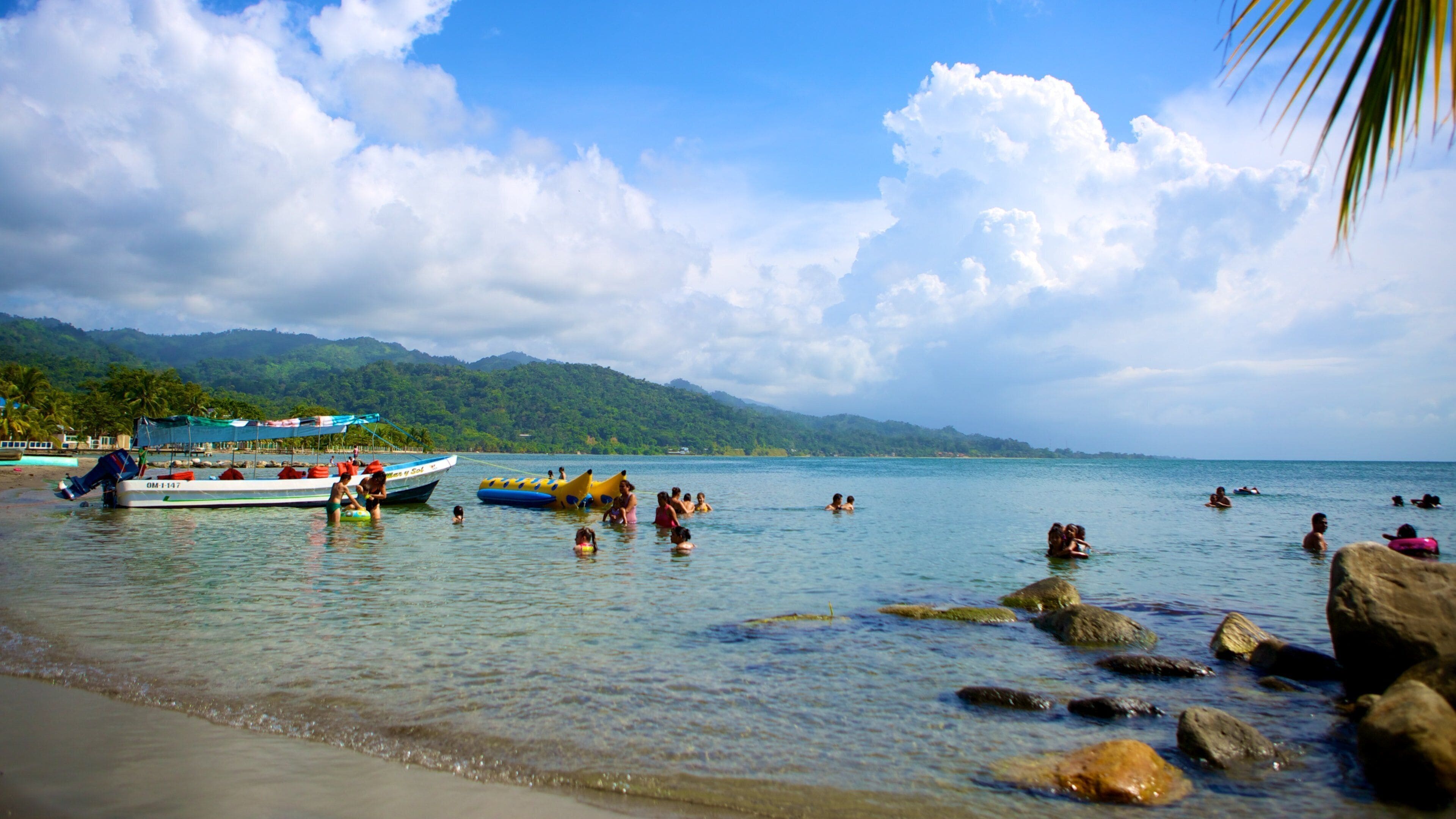Una playa tropical con agua cristalina, rocas y barcos.
