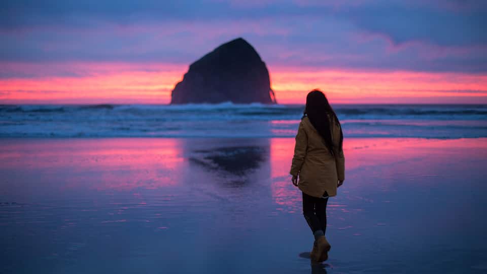 A girl walking to the haystack rock on Cape Kiwanda Beach during awesome sunset near Pacific City, Oregon