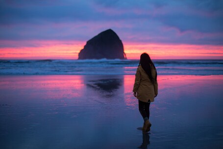 A person walking on a beach with a large rock formation in the distance during sunset.