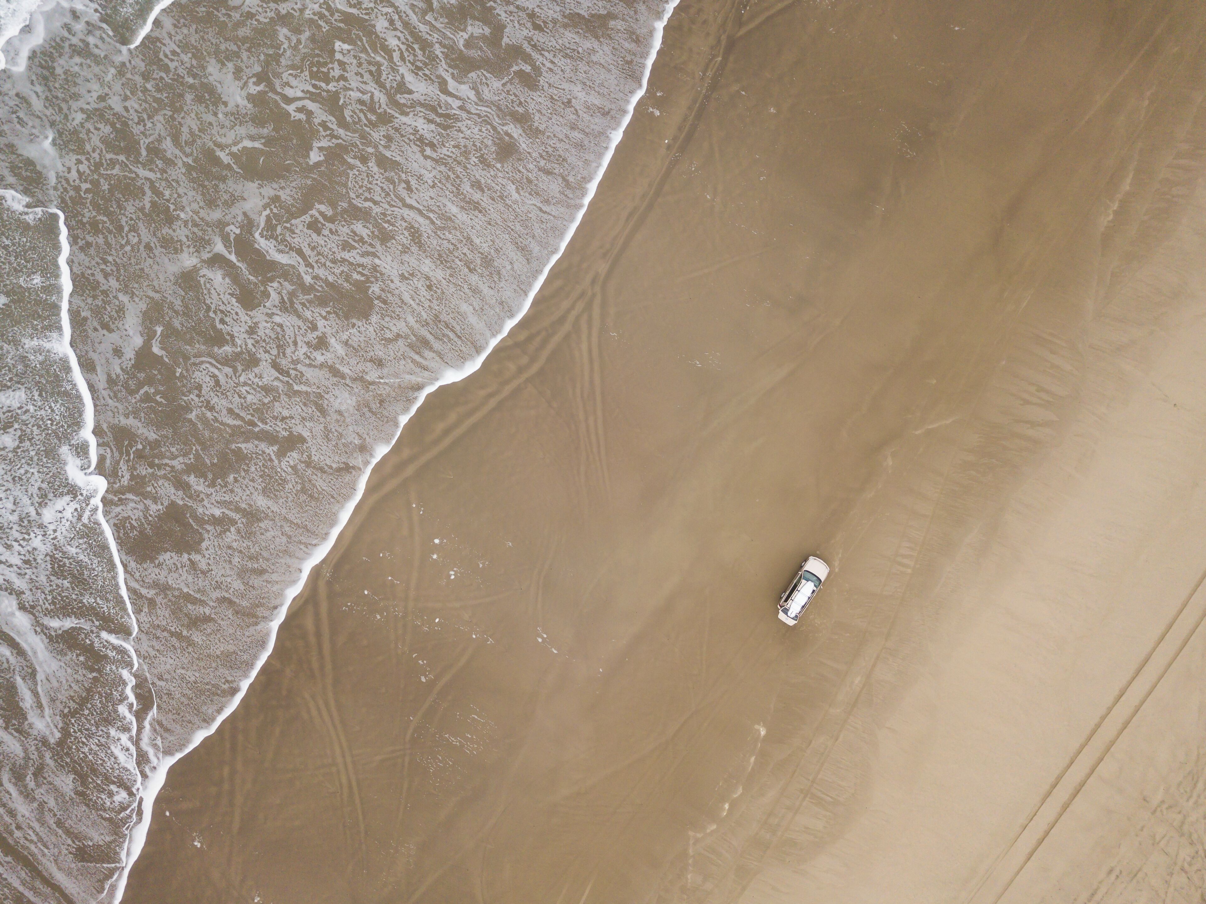 A sandy beach with gentle waves and a single vehicle parked on the shore.