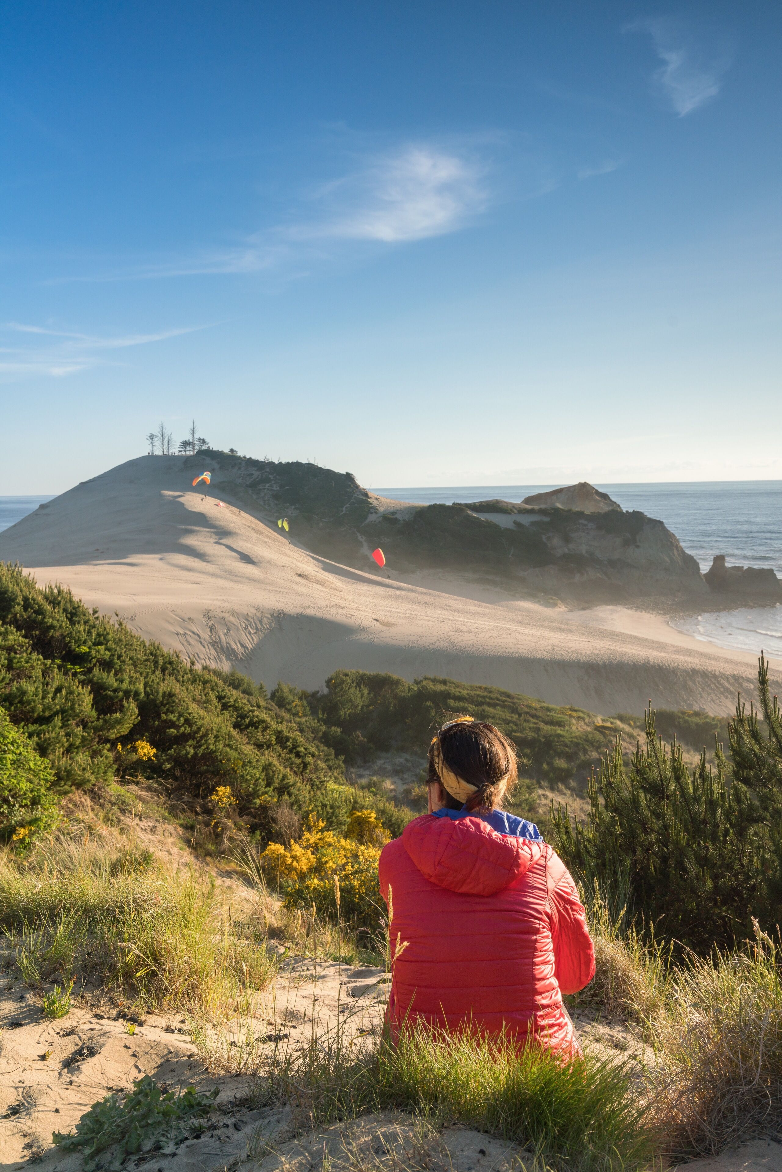 My girlfriend sits on the dunes in Oregon as she watches paragliders flying along the Pacific Ocean during golden hour! I should get the photo spot with #BvSCrete because traveling and photography are my passion. I use my camera as a tool to document this amazing life and great people!