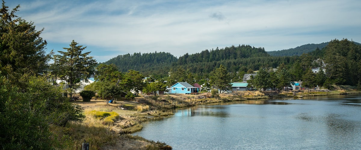 A calm lake with houses on the shore, surrounded by dense forest and hills.