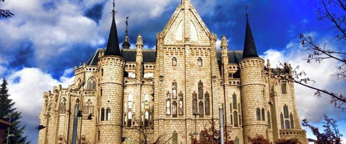 A large, historic stone building with multiple towers and spires, surrounded by a paved area with benches.