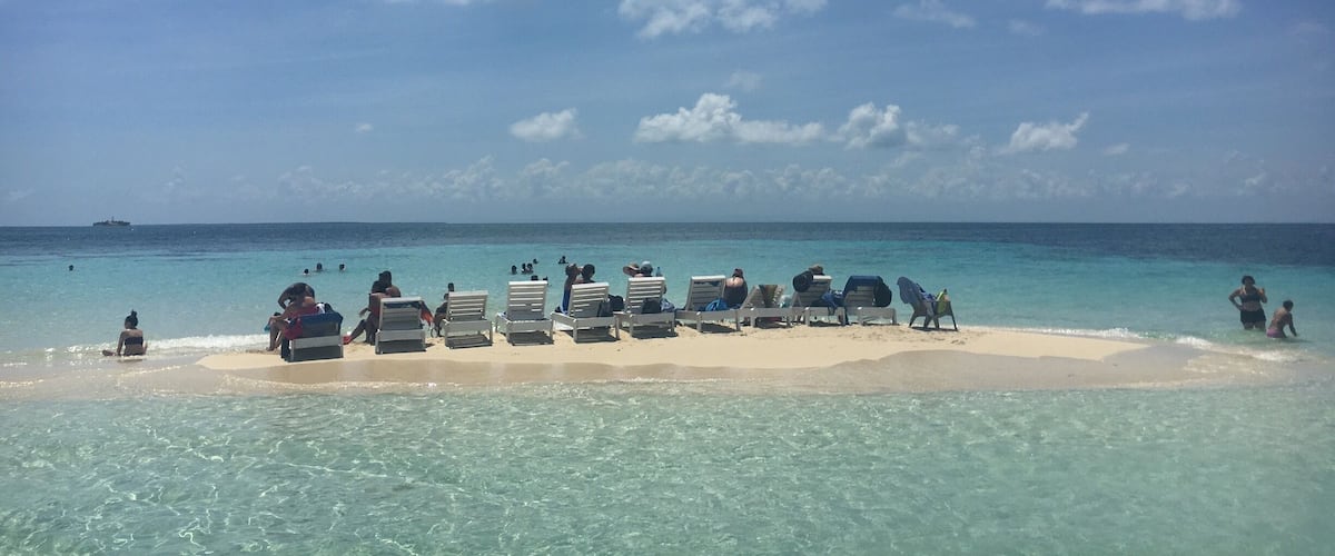 A beach with clear turquoise water, white sand, and a few people in the water.