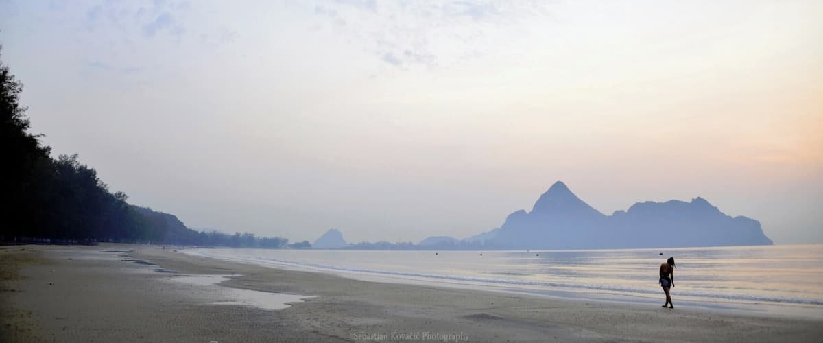 A beach with a person walking, calm water, and distant mountains.