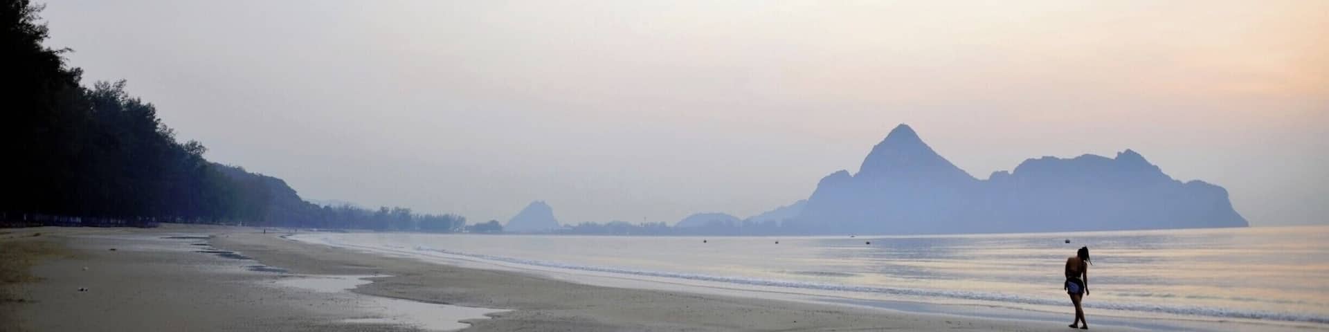 A beach with a person walking, calm water, and distant mountains.
