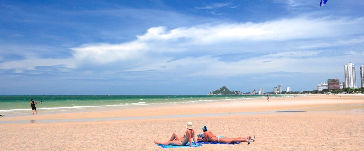 A beach with people sunbathing and a person kite surfing.