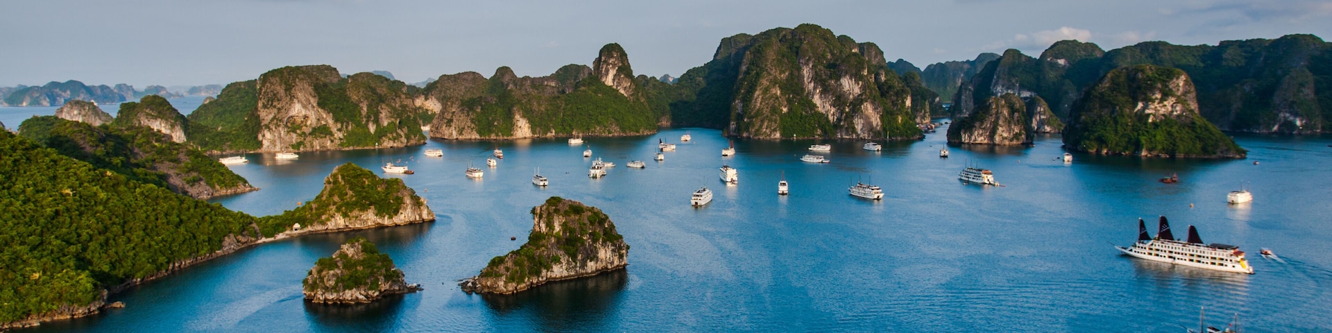 Uma área costeira com diversos barcos, ilhas verdes exuberantes e um mar azul cristalino.