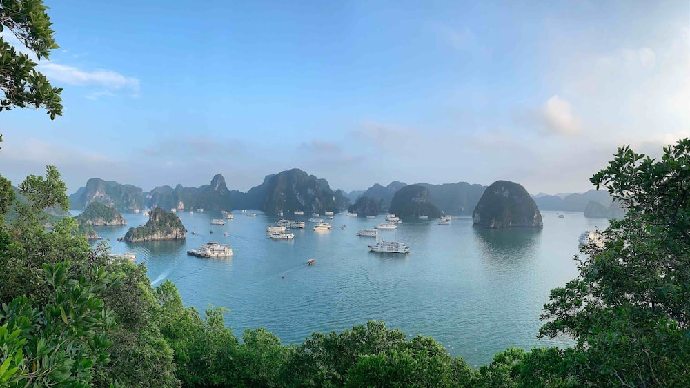 A coastal scene with numerous boats on calm waters, surrounded by lush green islands and rocky formations.