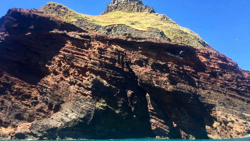 Eine felsige Küstenlandschaft mit einer markanten Klippe und türkisfarbenem Wasser.