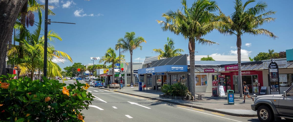 A street lined with palm trees and various shops, including a health spa and a surf shop.
