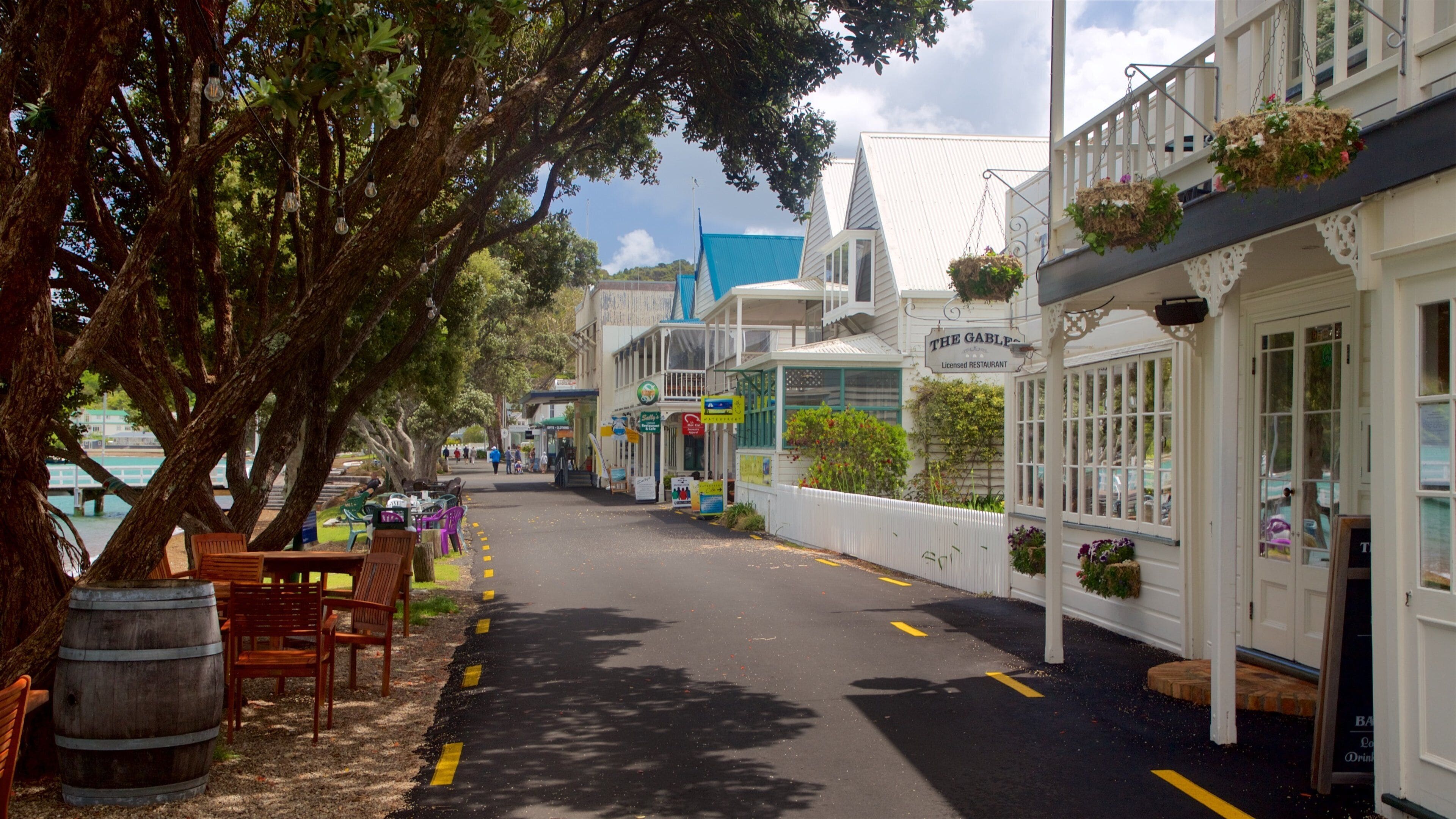 A tree-lined street with outdoor seating, a blue-roofed building, and hanging flower baskets.