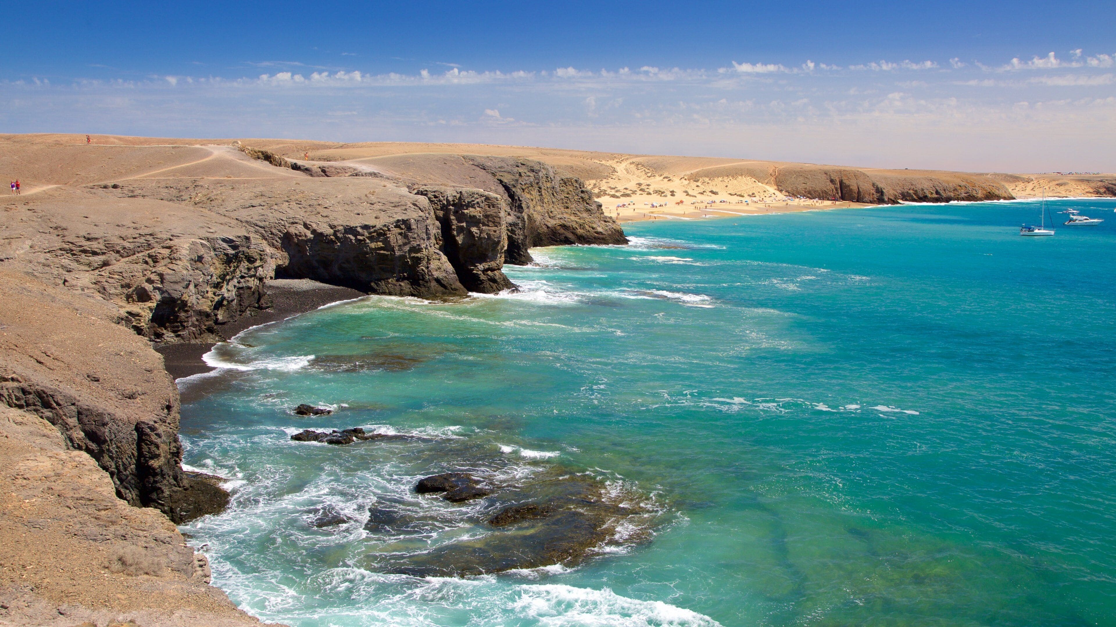 A coastal landscape with rocky cliffs, clear turquoise waters, and a sandy beach.