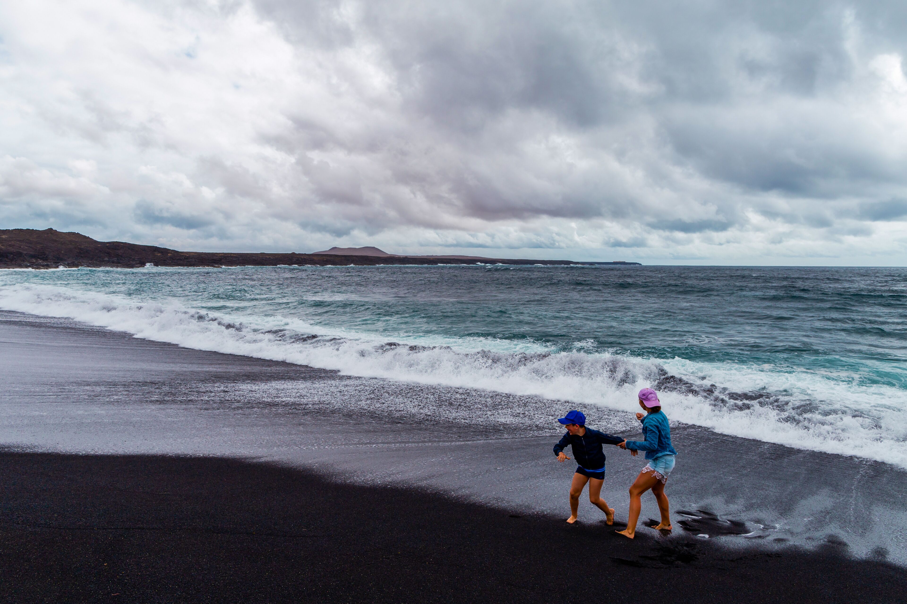 Una playa con arena oscura y olas rompiendo en la orilla.