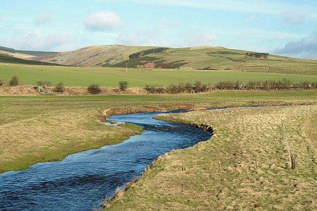 A river winding through a grassy valley with rolling hills in the background.
