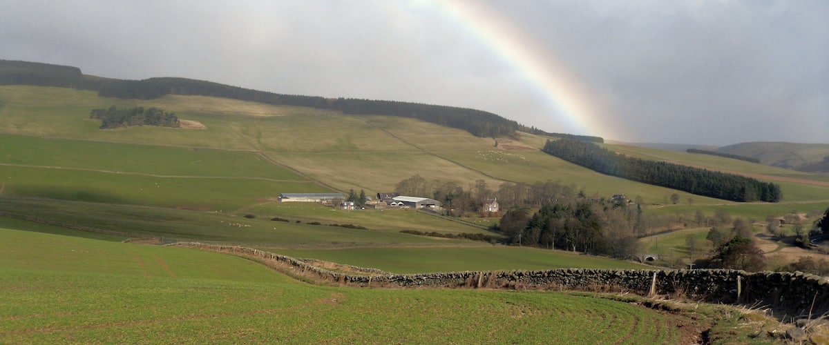 A rural landscape with rolling hills, a rainbow, and scattered buildings.