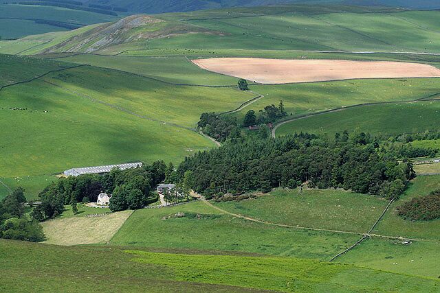 A rural landscape with rolling hills, a farmhouse, and a patchwork of fields.