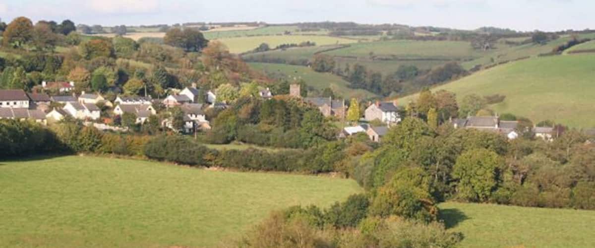 A rural landscape with rolling hills, scattered houses, and a clear sky.