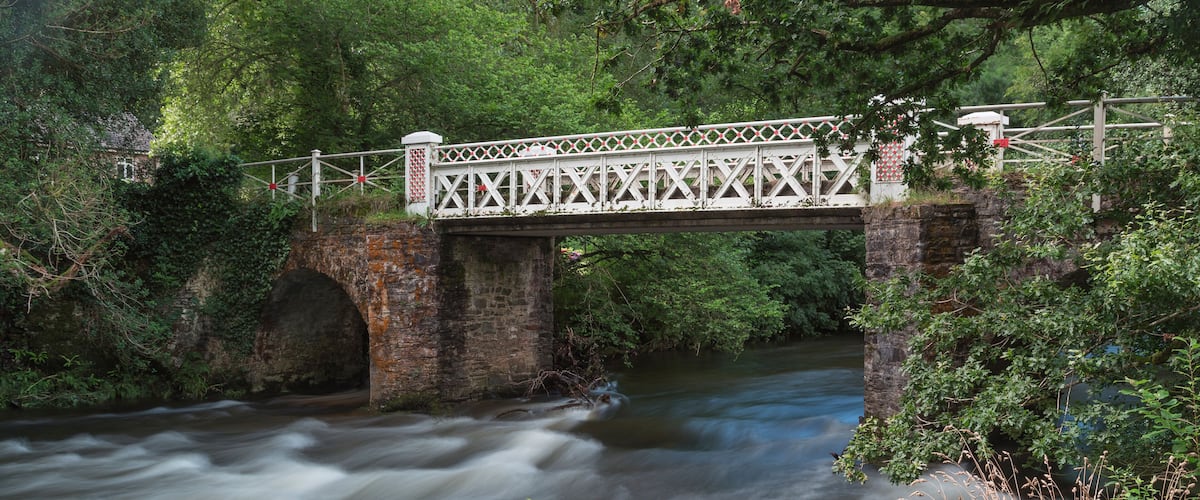 A stone bridge over a flowing river surrounded by lush greenery.