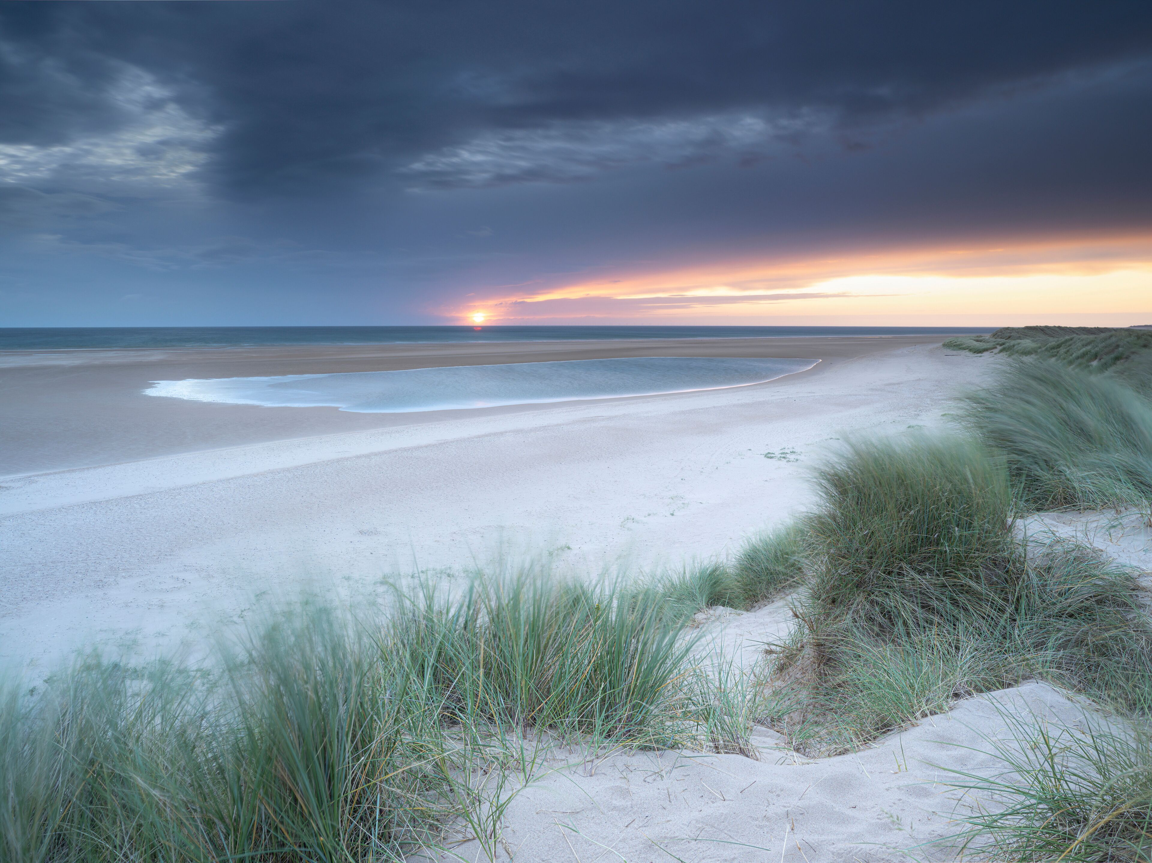 Una playa con dunas de arena y un atardecer sobre el océano.