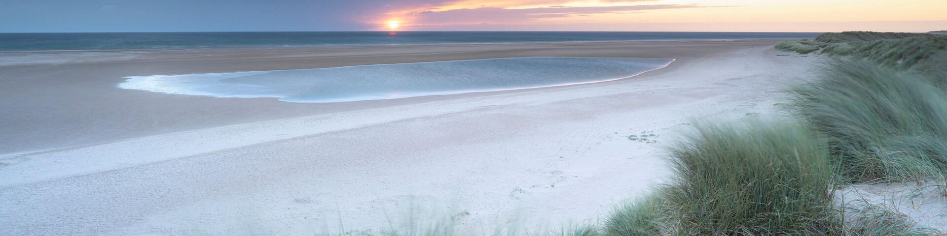 Una playa con dunas de arena y un atardecer sobre el océano.