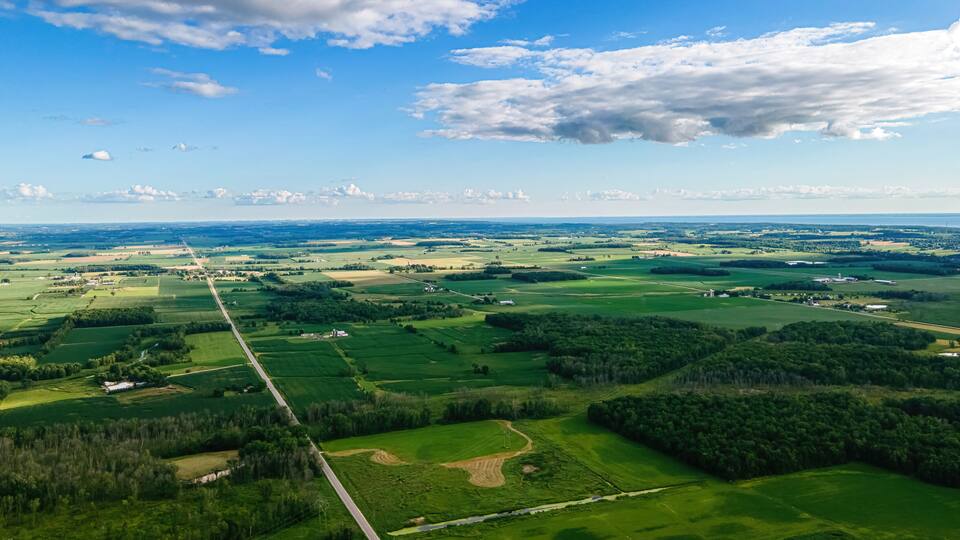 A vast agricultural landscape with fields, roads, and scattered buildings under a clear sky.
