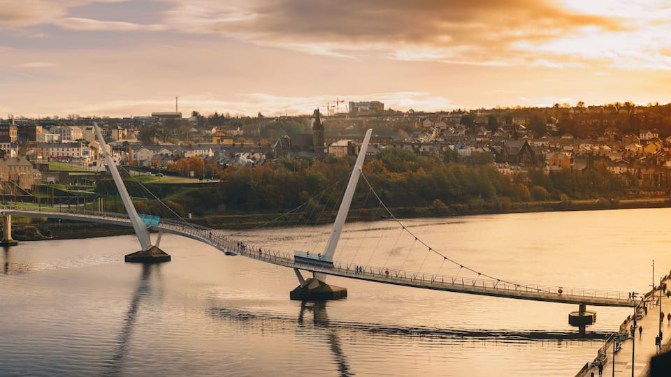 A suspension bridge over a river with a town in the background.