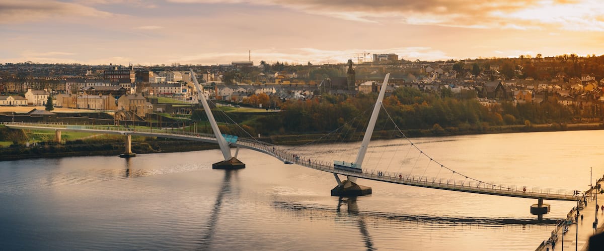 A suspension bridge over a river with a town in the background.